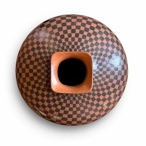 May include: A handcrafted ceramic vase with a unique design. The vase features a checkerboard pattern in shades of brown and black. The vase has a square opening with a dark interior, and is ideal for home decor.