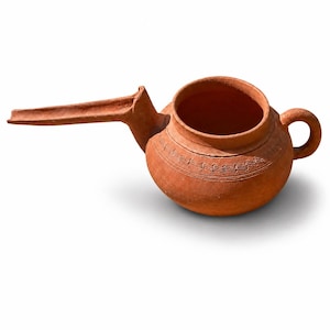 May include: A terracotta ceramic pitcher with a long spout and a small handle. The pitcher has a round body with decorative etched lines around the top. The color is a warm reddish-brown.