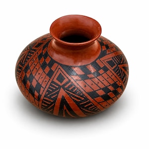 May include: A handcrafted, round terracotta-colored pottery vase with a wide opening. The vase features a geometric pattern in black, covering the body. The design includes diamond and triangular shapes. The vase is likely used for decorative purposes.