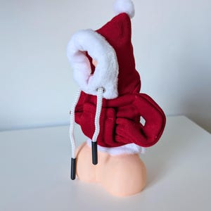 Pu&ograve; includere: Felpa con cappuccio rossa con bordino in pelliccia bianca e coulisse bianca. La felpa &egrave; su una figura color carne.