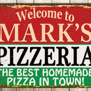May include: A vintage-style sign with red, white and green colours. The sign reads "Welcome to Mark's Pizzeria The Best Homemade Pizza in Town!"