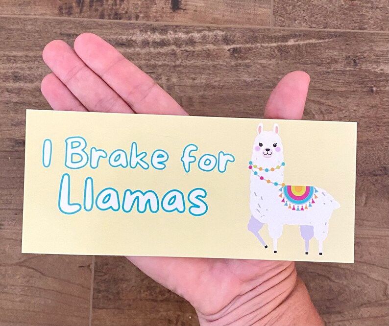 May include: A yellow bumper sticker with the text "I Brake for Llamas" in blue lettering. A cartoon llama with a colourful saddle and beaded necklace is on the right side of the sticker.
