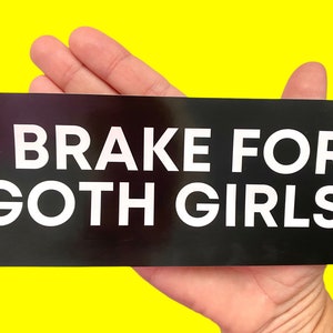 May include: Black and white bumper sticker with the text "I Brake For Goth Girls".