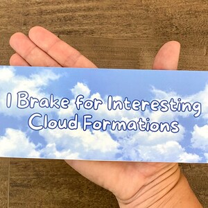 May include: A blue and white bumper sticker with the text "I Brake for Interesting Cloud Formations".