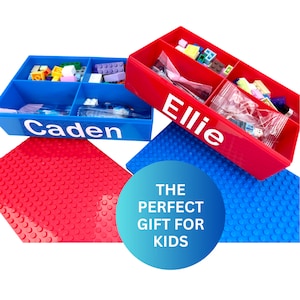 May include: Two blue and red plastic storage boxes with dividers for Lego bricks. The boxes are labeled "Caden" and "Ellie". The boxes are sitting on top of blue and red Lego base plates. The text "THE PERFECT GIFT FOR KIDS" is written in white on a blue circle.