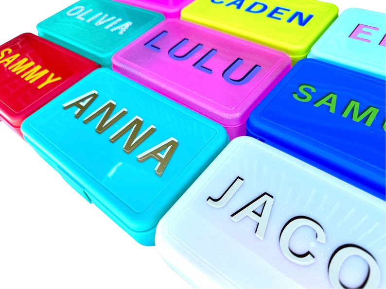 May include: A set of colorful rectangular lunch boxes with names printed on them. The names include Olivia, Caden, Lulu, Sammy, Anna, Sam, and Jacob.