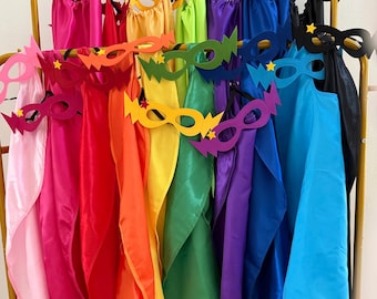 May include: A collection of satin superhero capes and felt masks in a rainbow of colours including pink, red, orange, yellow, green, blue, purple, and black. Each mask features a lightning bolt design on the sides and a small yellow star accent.