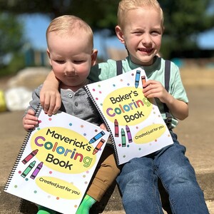 May include: Two children holding spiral-bound coloring books. The books have colorful crayon illustrations and the text "Maverick's Coloring Book" and "Baker's Coloring Book". The text "Created just for you" is also visible.