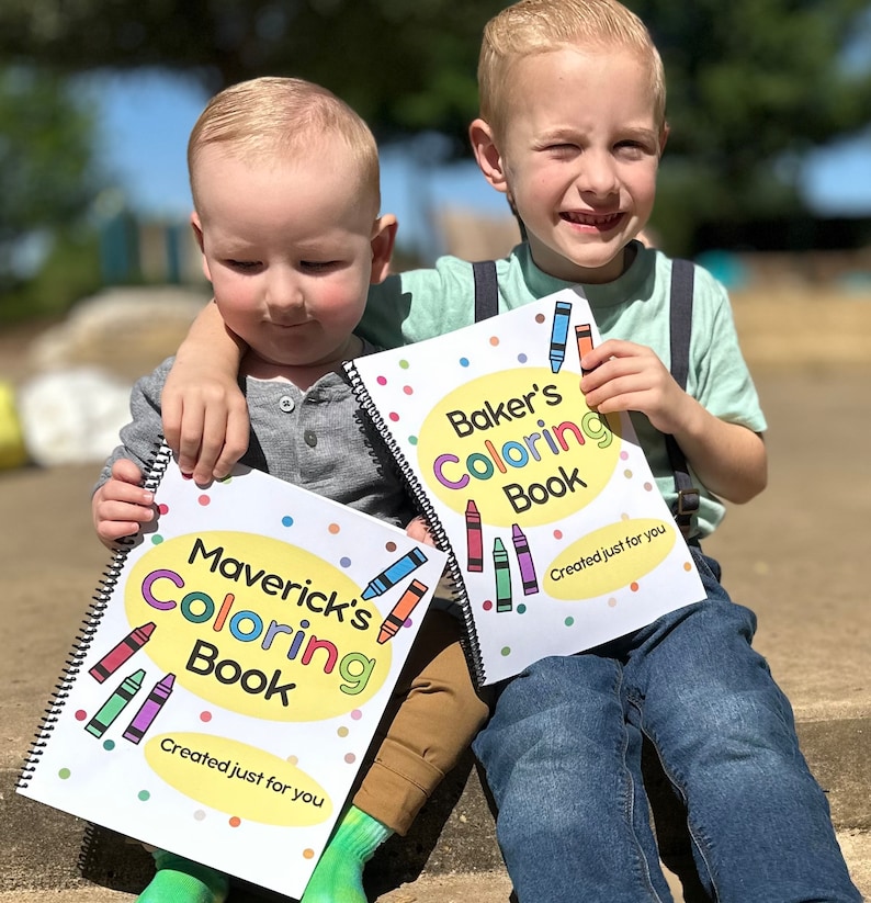 May include: Two children holding spiral-bound coloring books. The books have colorful crayon illustrations and the text "Maverick's Coloring Book" and "Baker's Coloring Book". The text "Created just for you" is also visible.