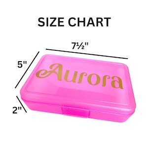 May include: Pink plastic pencil box with a gold glitter finish. The box is 7 1/2 inches long, 5 inches wide, and 2 inches tall. The name "Aurora" is printed in gold on the top of the box.