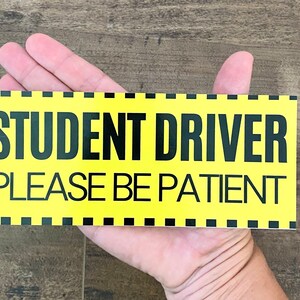 May include: Yellow sign with black text that reads "Student Driver Please Be Patient".