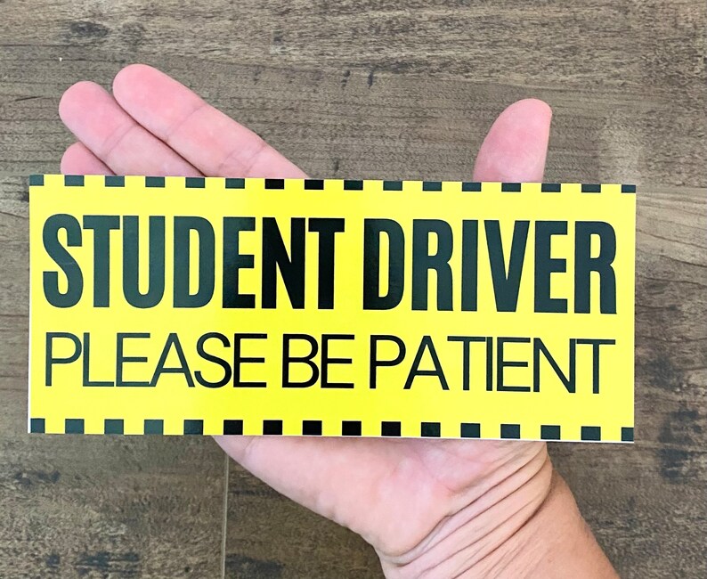 May include: Yellow sign with black text that reads "Student Driver Please Be Patient".