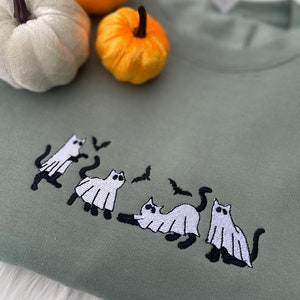 May include: A sage green sweatshirt with an embroidered design of four white cats dressed as ghosts with black bats flying above them.