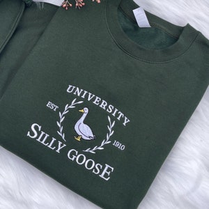 May include: A dark green sweatshirt with a white embroidered design. The design features a goose with the text "University Silly Goose Est 1910".