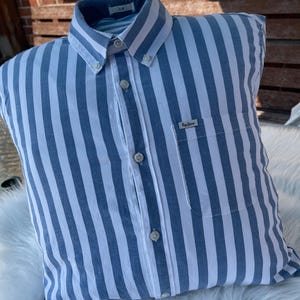 May include: A blue and white striped pillow with a button closure and a small logo that says "Original Penguin" in the lower right corner.