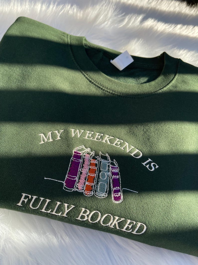 Green sweatshirt with “My Weekend is Fully Booked” embroidered book stack