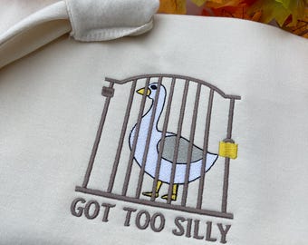 May include: A cream-colored sweatshirt with an embroidered image of a goose in a cage with the text "GOT TOO SILLY".