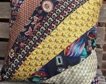 May include: Square decorative pillow with a patchwork design. The pillow features diagonal stripes of various patterned fabrics, including floral, geometric, and abstract designs in navy, yellow, red, and teal. The pillow is placed on a wooden surface.