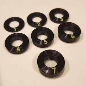 May include: Seven black plastic rings with numbers 1 through 7 printed in yellow on the top of each ring.