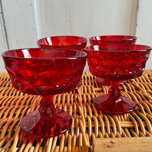 Peut inclure: Quatre coupes à pied en verre rouge avec un motif en diamant. Les coupes sont posées sur une surface en osier tressé.
