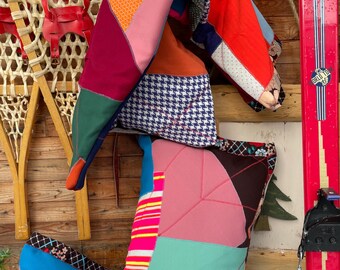 May include: A selection of vibrant patchwork cushions and a folded quilt. The cushions display geometric patterns in pink, teal, and blue, with a houndstooth design. A pair of vintage red skis and a wooden snowshoe are in the background.
