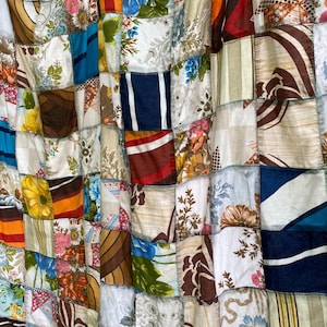 Peut inclure: Une courtepointe en patchwork composée de divers carrés de tissu présentant des motifs variés, notamment des imprimés floraux, des rayures et des couleurs unies dans des tons de bleu, marron, orange, jaune et blanc, assemblés par des coutures sombres.