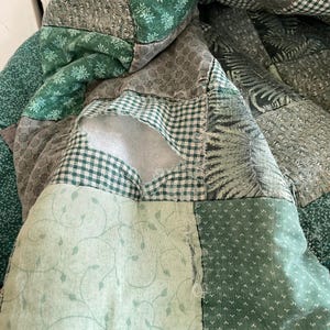 K&ouml;nnte beinhalten: Eine gr&uuml;ne Patchwork-Decke mit verschiedenen Mustern, darunter Blumen, geometrische Muster und Karos. Die Decke hat ein Loch in der Mitte.