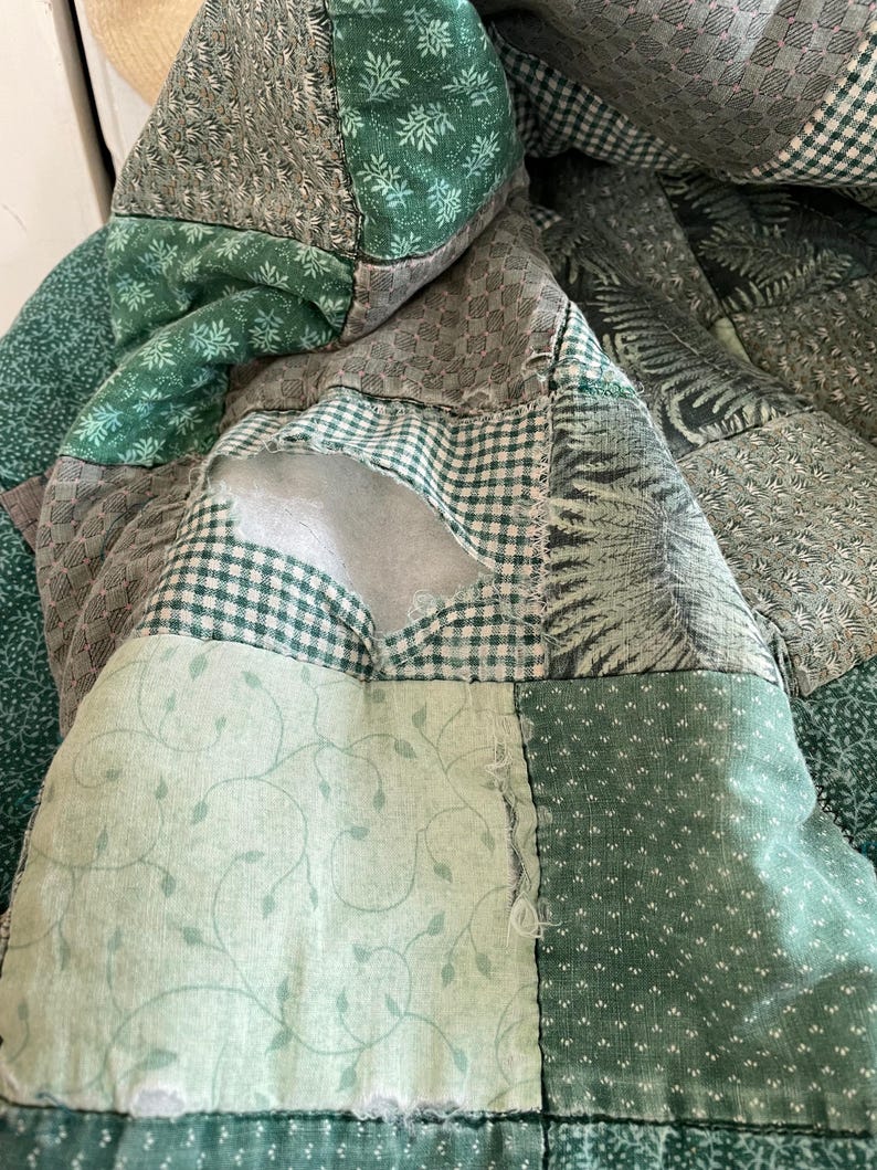 K&ouml;nnte beinhalten: Eine gr&uuml;ne Patchwork-Decke mit verschiedenen Mustern, darunter Blumen, geometrische Muster und Karos. Die Decke hat ein Loch in der Mitte.
