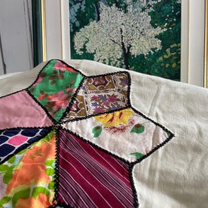 Peut inclure: Gros plan sur un bloc de quilt en forme d'étoile avec divers motifs de tissus, notamment des motifs floraux et rayés. Le bloc de quilt est cousu sur un fond crème et bordé de coutures noires. Une peinture encadrée d'un arbre est en arrière-plan.