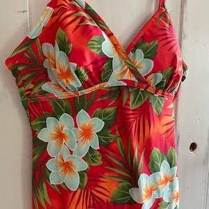 May include: A red swimsuit with a tropical floral print featuring white flowers and green leaves.