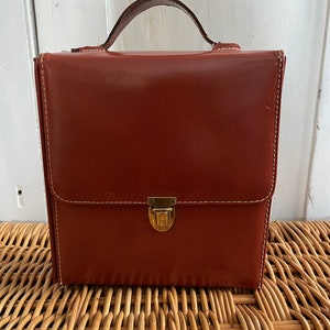 May include: A brown leather briefcase with a brass clasp and a top handle.