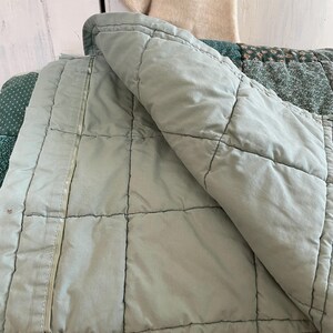 K&ouml;nnte beinhalten: Eine gesteppte Tagesdecke in Salbeigr&uuml;n mit einem wei&szlig;en Rei&szlig;verschlussdetail. Die Decke ist in der H&auml;lfte gefaltet und der Rei&szlig;verschluss ist an der Seite sichtbar.