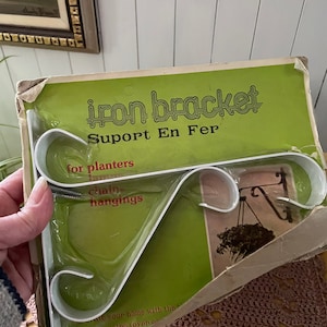 Peut inclure: Un support en métal blanc pour suspendre des pots de fleurs, des chaînes ou d'autres objets. L'emballage est vert et porte le texte "iron bracket Support En Fer".