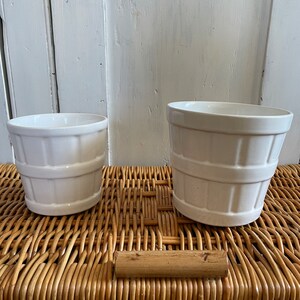 May include: Two white ceramic plant pots with a ribbed design. The pots are sitting on a woven wicker surface.