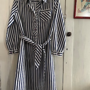 May include: A long-sleeved, white and navy blue striped dress with a button-up front and a tie belt. The dress has a pocket on the left side of the chest.