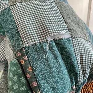 K&ouml;nnte beinhalten: Eine gr&uuml;ne Patchwork-Decke mit verschiedenen floralen und karierten Mustern. Die Decke hat einen kleinen Riss in einem der Quadrate.