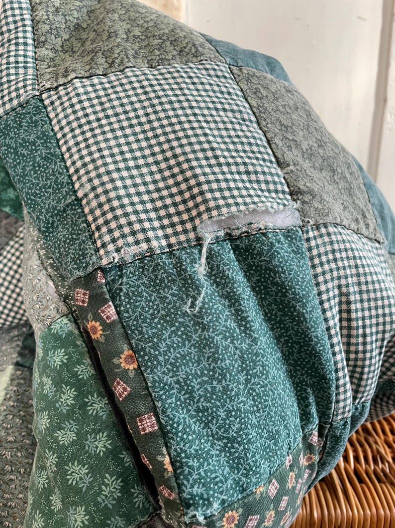 K&ouml;nnte beinhalten: Eine gr&uuml;ne Patchwork-Decke mit verschiedenen floralen und karierten Mustern. Die Decke hat einen kleinen Riss in einem der Quadrate.