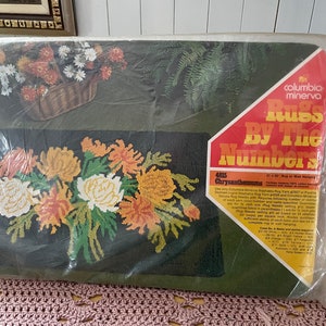 Peut inclure: Un kit de fabrication de tapis à crocheter avec un motif de chrysanthèmes. Le kit comprend une toile pré-imprimée, de la laine et une aiguille. Le kit est intitulé "Rugs By The Numbers" et "Chrysanthemums".