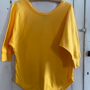 Op de afbeelding: Een geel, kortmouwig, loszittend katoenen T-shirt met een ronde hals.