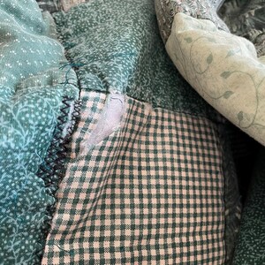 K&ouml;nnte beinhalten: Eine Patchwork-Decke aus gr&uuml;nem und wei&szlig;em Stoff mit einem karierten Muster. Die Decke besteht aus verschiedenen Stoffst&uuml;cken, die zusammengen&auml;ht wurden.