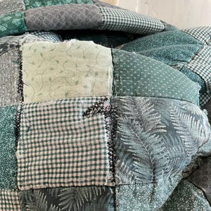 K&ouml;nnte beinhalten: Eine gr&uuml;ne Patchwork-Decke mit verschiedenen Mustern, darunter Farne, Bl&auml;tter und Gingham. Die Decke ist aus verschiedenen Gr&uuml;nt&ouml;nen gefertigt und hat einen rustikalen, handgefertigten Look.