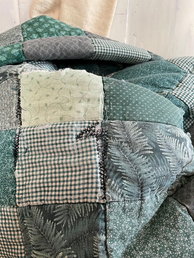 K&ouml;nnte beinhalten: Eine gr&uuml;ne Patchwork-Decke mit verschiedenen Mustern, darunter Farne, Bl&auml;tter und Gingham. Die Decke ist aus verschiedenen Gr&uuml;nt&ouml;nen gefertigt und hat einen rustikalen, handgefertigten Look.