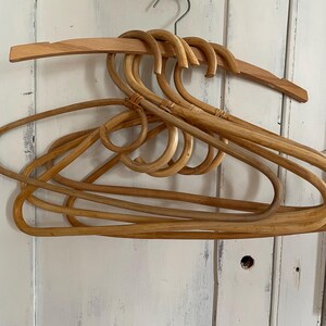 Peut inclure: Plusieurs cintres en bois de couleur marron clair. Les cintres sont en rotin tressé et ont un design incurvé. Le cintre supérieur est en bois massif. Les cintres sont suspendus à un crochet en métal.