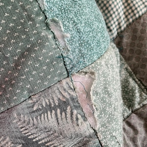 K&ouml;nnte beinhalten: Eine Nahaufnahme einer gr&uuml;n-wei&szlig;en Patchwork-Decke mit ausgefranstem Rand. Die Decke besteht aus verschiedenen Stoffen mit verschiedenen Mustern, darunter Blumen, geometrische Muster und Paisley.