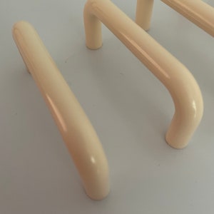 May include: Three off-white plastic cabinet door handles with a rounded, D-shaped design.