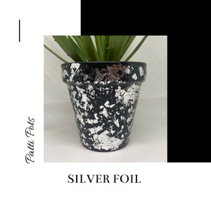 May include: Black terracotta planter pot with silver foil accents. The pot is decorated with a crackled finish and has a plant inside.