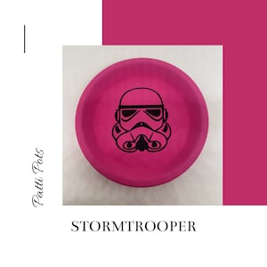 May include: A pink round dish with a black and white image of a Star Wars Stormtrooper. The dish says "STORMTROOPER" in black text.