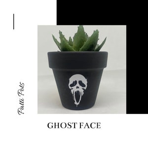 May include: Black terracotta planter with a white Ghostface skull design, featuring a succulent plant.