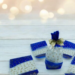 Peut inclure: Quatre sacs cadeaux bleus et blancs avec des étoiles dorées et un ruban doré sur une surface en bois blanc. Les sacs cadeaux sont remplis de papier de soie blanc et d'étoiles dorées.