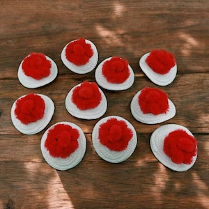 Puede incluir: Diez círculos de fieltro blanco con pompones rojos en el centro. Los círculos están dispuestos en semicírculo sobre una superficie de madera.
